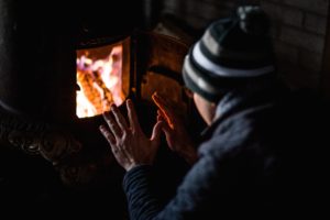 Man sits in front of a fiery furnace, warming hands